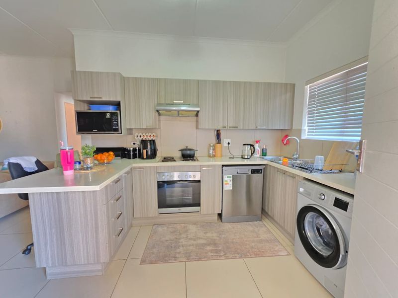Modern kitchen featuring light wood-grain cabinetry, built-in oven, hob, extractor fan, integrated dishwasher, and tiled flooring with a functional layout.