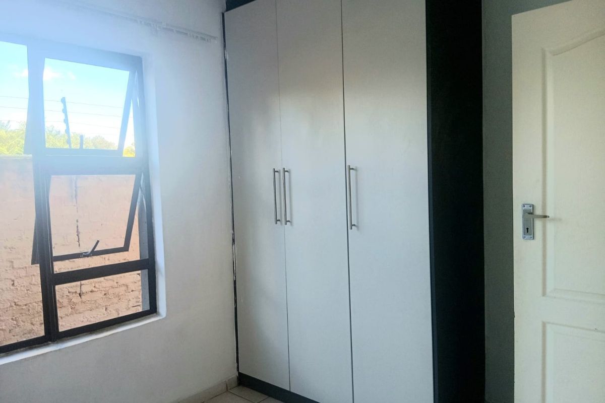 A clean, empty bedroom featuring a modern built-in wardrobe with white doors, tiled flooring, and an aluminium window frame.