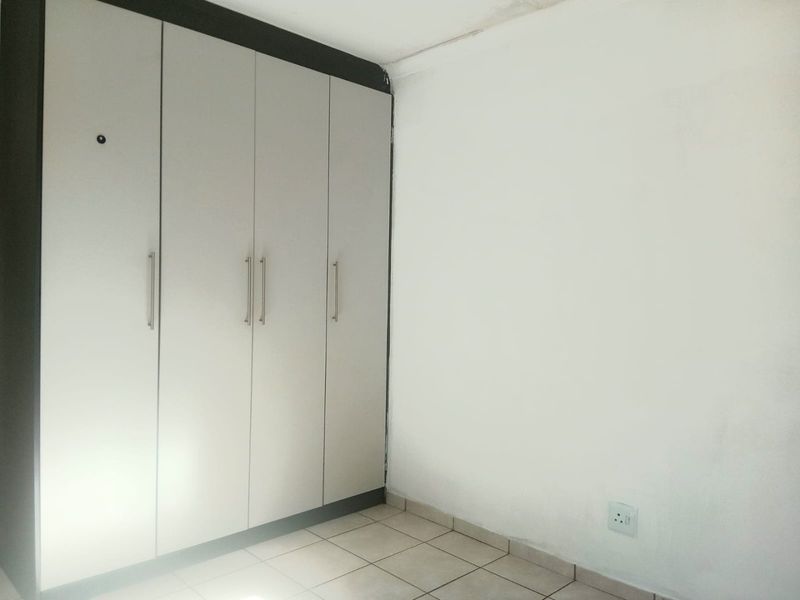 A vacant bedroom featuring built-in cupboards and tiled flooring, showing signs of minor wear on the walls and ceiling.