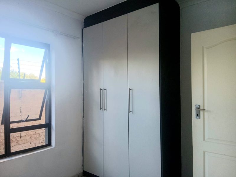 A bright bedroom featuring a modern built-in wardrobe with contrasting black and white finishes and an aluminium window frame.