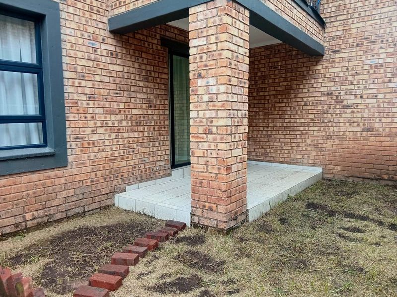 A ground floor patio area featuring exposed brickwork, a tiled floor, and a brick support pillar, providing direct access to the apartment interior.