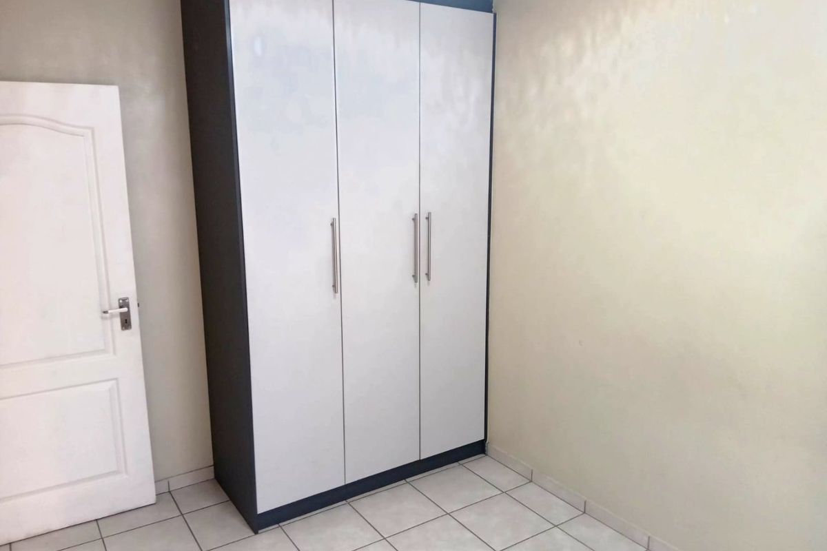 A clean, empty bedroom featuring neutral tiled flooring and a modern built-in wardrobe with white doors and dark framing.