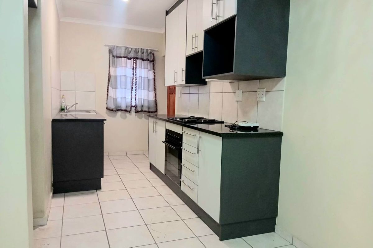 A clean, functional kitchen featuring modern two-tone cabinetry, granite countertops, a built-in oven and hob, and tiled flooring throughout.