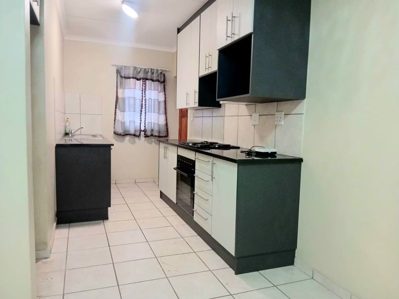 A clean, functional kitchen featuring modern two-tone cabinetry, granite countertops, a built-in oven and hob, and tiled flooring throughout.