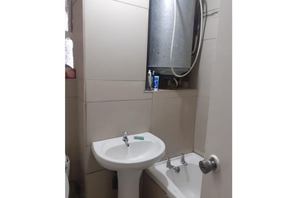 Compact bathroom featuring a pedestal basin, bathtub, and wall-mounted electric water heater with exposed plumbing.