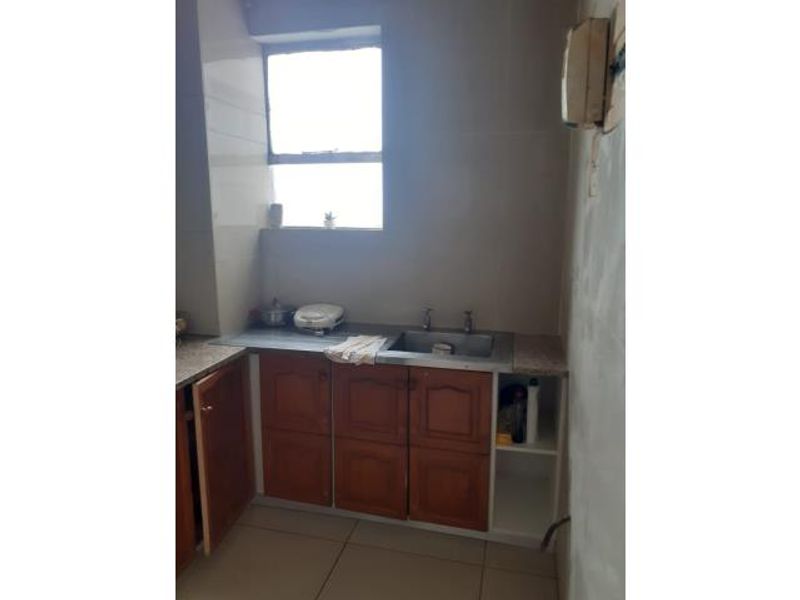 A compact kitchen area featuring wooden cabinetry, a stainless steel sink, and tiled finishes, currently requiring cosmetic updates and wall finishing.