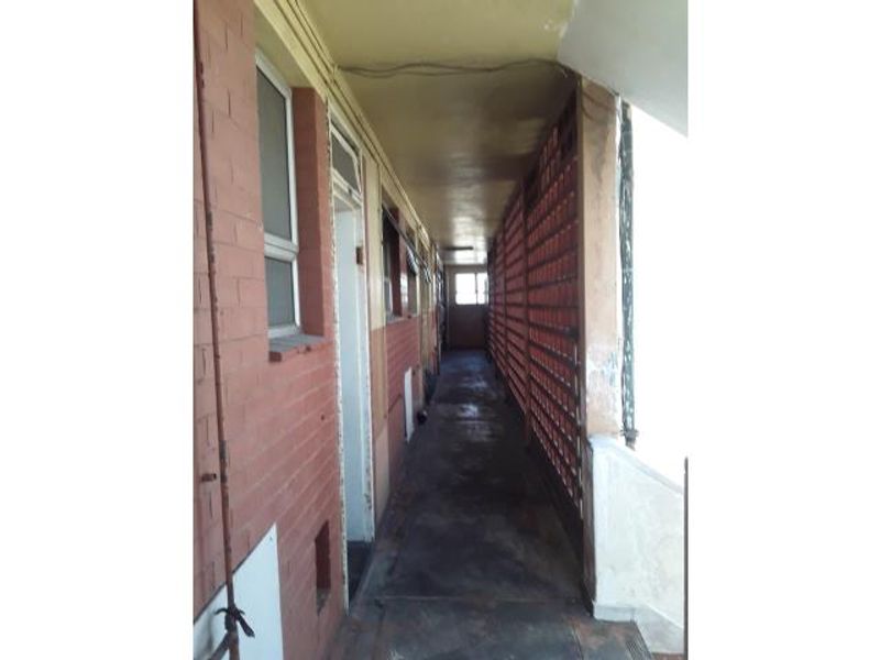An exterior apartment building corridor featuring brick walls, concrete flooring, and a metal security screen.
