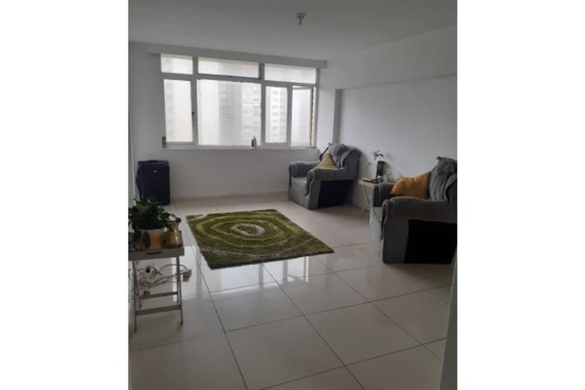 A bright living room featuring large windows and neutral tiled flooring, offering a clean and functional space ready for personalization.