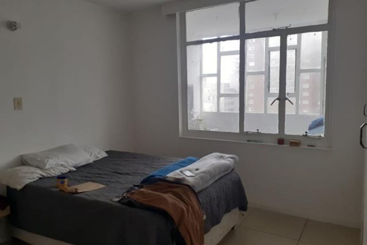 A simple bedroom featuring large windows that provide natural light and tiled flooring throughout.