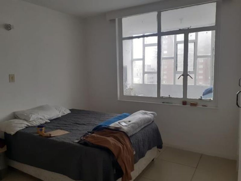 A simple bedroom featuring large windows that provide natural light and tiled flooring throughout.