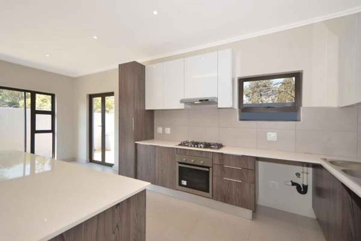 Modern kitchen featuring sleek two-tone cabinetry, stone countertops, built-in gas hob, oven, and extractor fan, with direct access to the outdoor area.