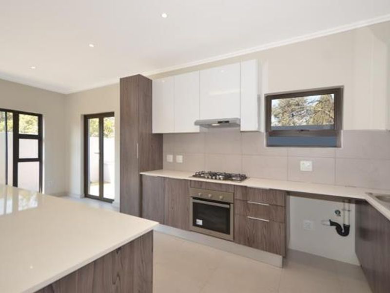Modern kitchen featuring sleek two-tone cabinetry, stone countertops, built-in gas hob, oven, and extractor fan, with direct access to the outdoor area.