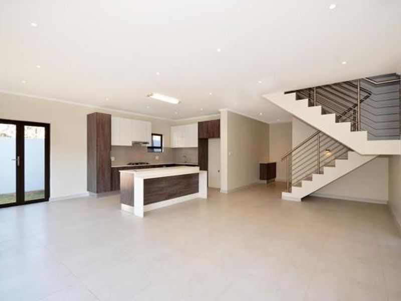 Spacious open-plan living area featuring a modern kitchen with island, tiled flooring, recessed lighting, and a contemporary staircase with metal balustrade.