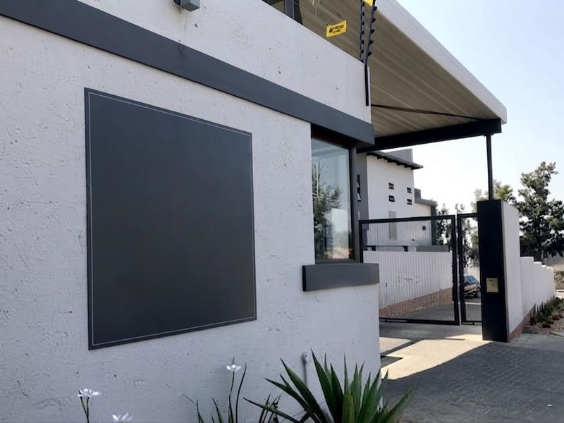 Front exterior view of the property featuring a modern textured facade, secure metal gate, and electric fencing along the roofline.