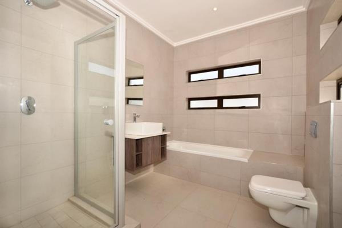 Modern bathroom featuring a glass shower enclosure, built-in bathtub, wall-mounted vanity with vessel sink, and wall-hung toilet with neutral tiled finishes.