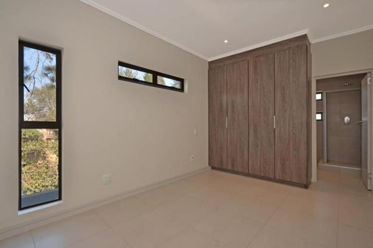 A modern, empty bedroom featuring built-in wood-finish cupboards, tiled flooring, recessed lighting, and direct access to an en-suite bathroom.