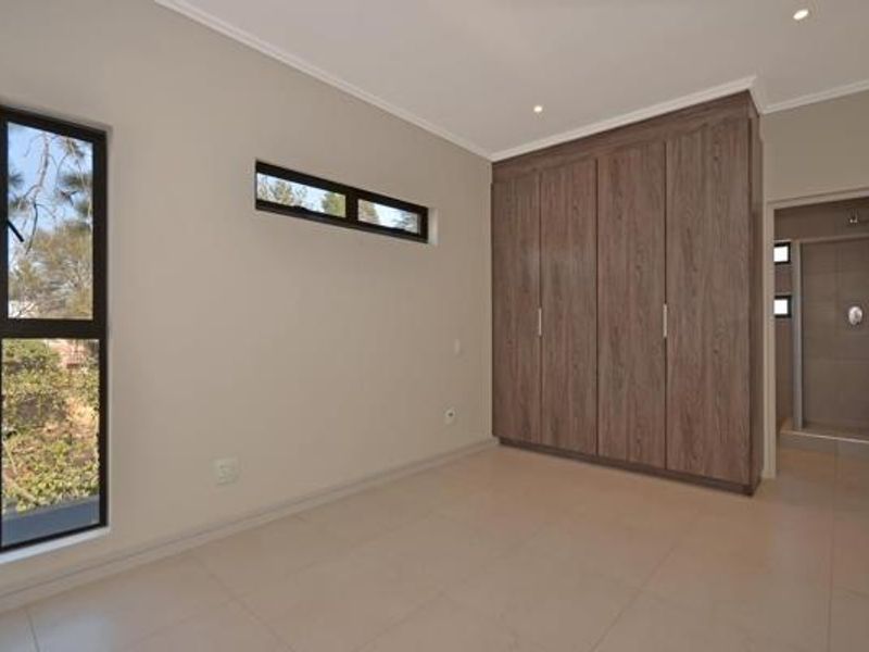 A modern, empty bedroom featuring built-in wood-finish cupboards, tiled flooring, recessed lighting, and direct access to an en-suite bathroom.