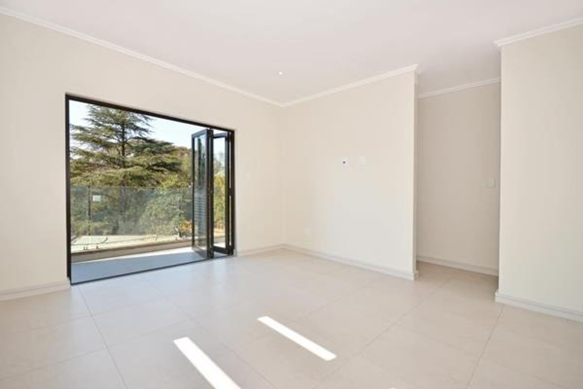 Bright and spacious living area featuring neutral tiled flooring, recessed lighting, and large bi-fold doors opening onto a balcony with a glass balustrade.