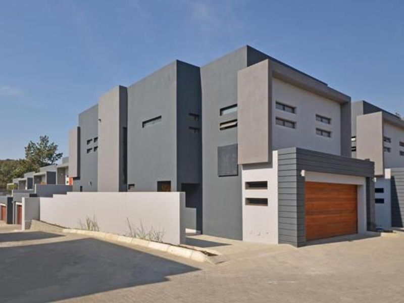 Modern multi-unit residential complex featuring contemporary grey and charcoal architectural design with timber-finish garage doors and paved driveway access.