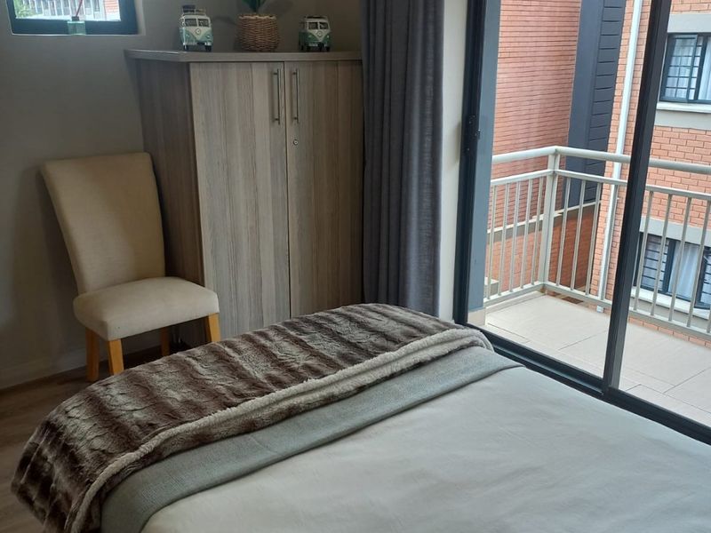 A well-lit bedroom featuring laminate flooring, a built-in cupboard, and a sliding glass door providing direct access to a private balcony.