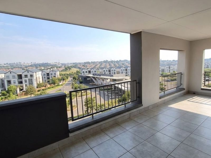 A spacious covered balcony featuring tiled flooring, a metal balustrade, and expansive views of the surrounding residential estate.