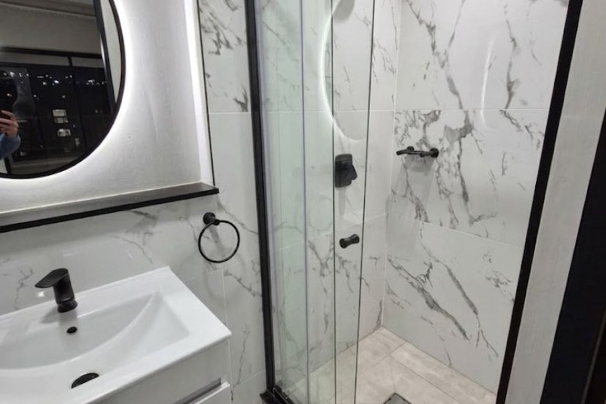 Modern bathroom featuring a sleek vanity, backlit mirror, and a glass-enclosed shower with contemporary marble-look wall tiles and matte black fixtures.