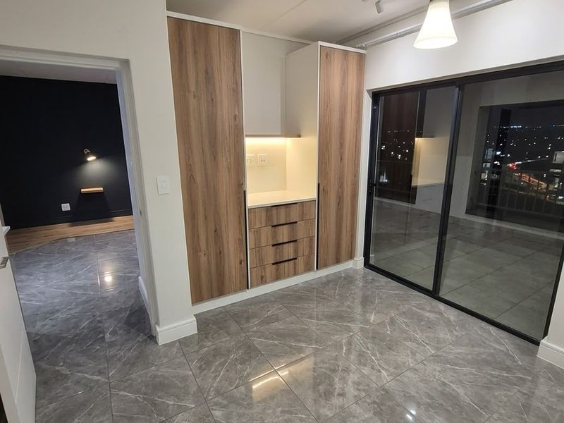 Modern open-plan living area featuring high-gloss marble-look floor tiles, sleek built-in cabinetry, and large sliding glass doors leading to a balcony.