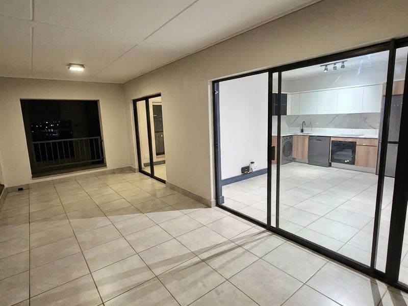 A spacious covered balcony with tiled flooring and sliding glass doors, offering a seamless transition to the modern kitchen area.