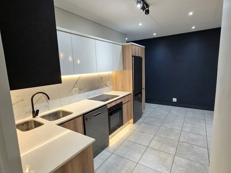 Modern kitchen featuring sleek two-tone cabinetry, stone countertops, marble-look splashback, integrated appliances, and contemporary track lighting in an open-plan layout.