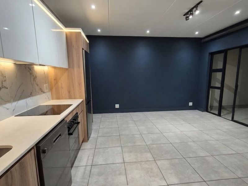 Modern open-plan kitchen and living area featuring sleek cabinetry, stone countertops, integrated appliances, tiled flooring, and large sliding glass doors leading outdoors.