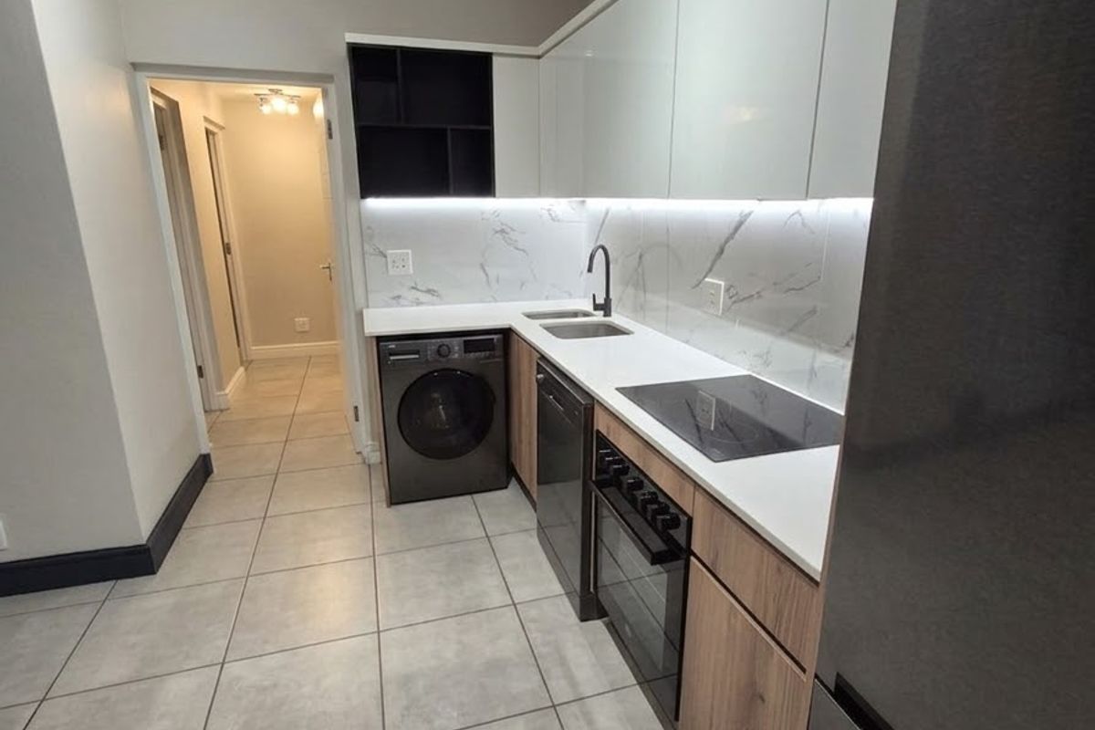 Modern kitchen featuring sleek white and wood-tone cabinetry, stone countertops, marble-look backsplash, integrated appliances, and contemporary track lighting.