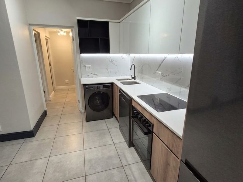 Modern kitchen featuring sleek white and wood-tone cabinetry, stone countertops, marble-look backsplash, integrated appliances, and contemporary track lighting.