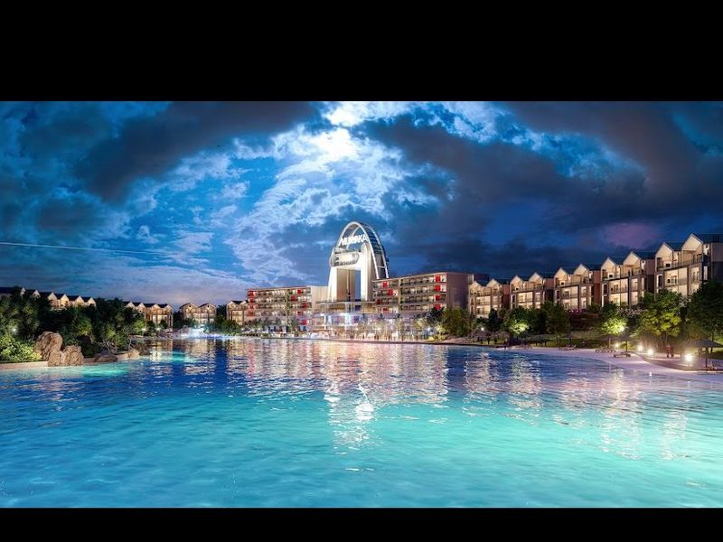 A night view of a large swimming pool area featuring a modern apartment complex and landscaped surroundings.