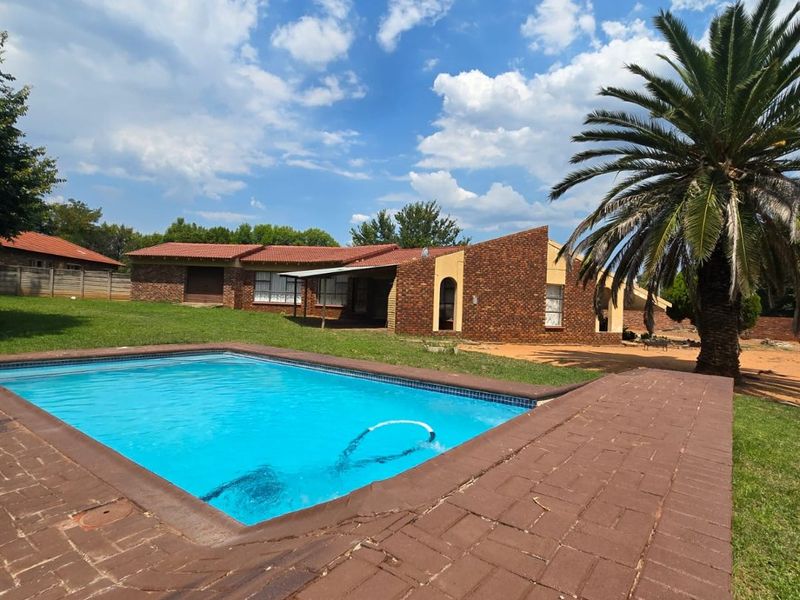 Outdoor pool area featuring a swimming pool with brick paving, set against a brick house facade and a spacious garden.