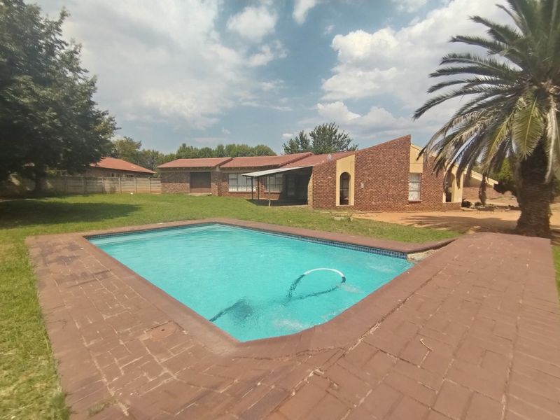 Spacious backyard featuring a swimming pool with brick paving, a covered patio area, and a face brick house exterior.