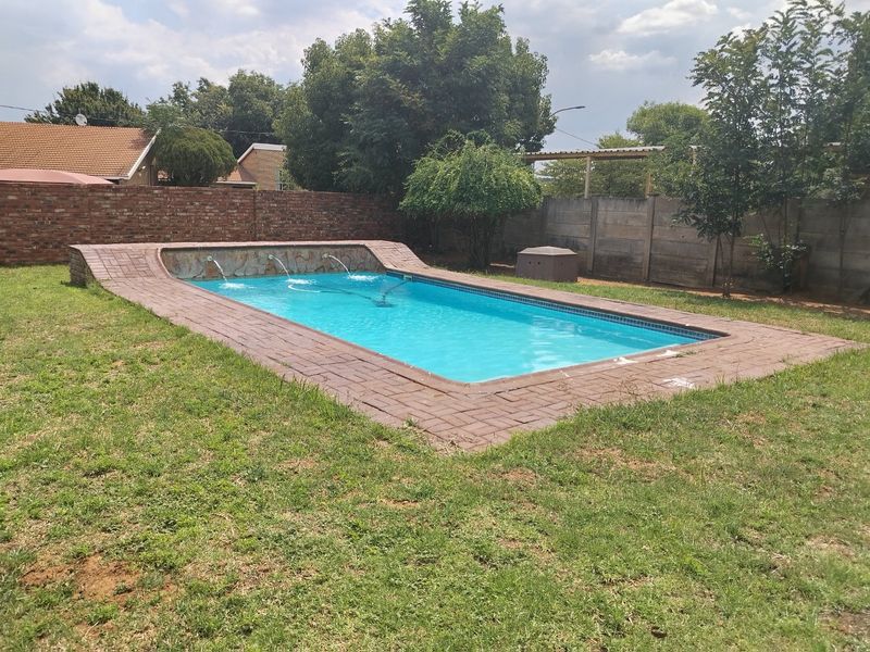 A rectangular swimming pool featuring a stone water feature, brick coping, and surrounding lawn area enclosed by brick and precast concrete boundary walls.