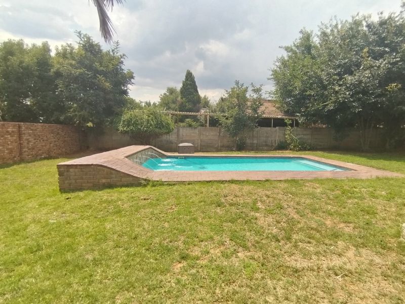 A backyard swimming pool featuring a brick water feature, surrounded by a lawn and enclosed by brick and precast concrete boundary walls.