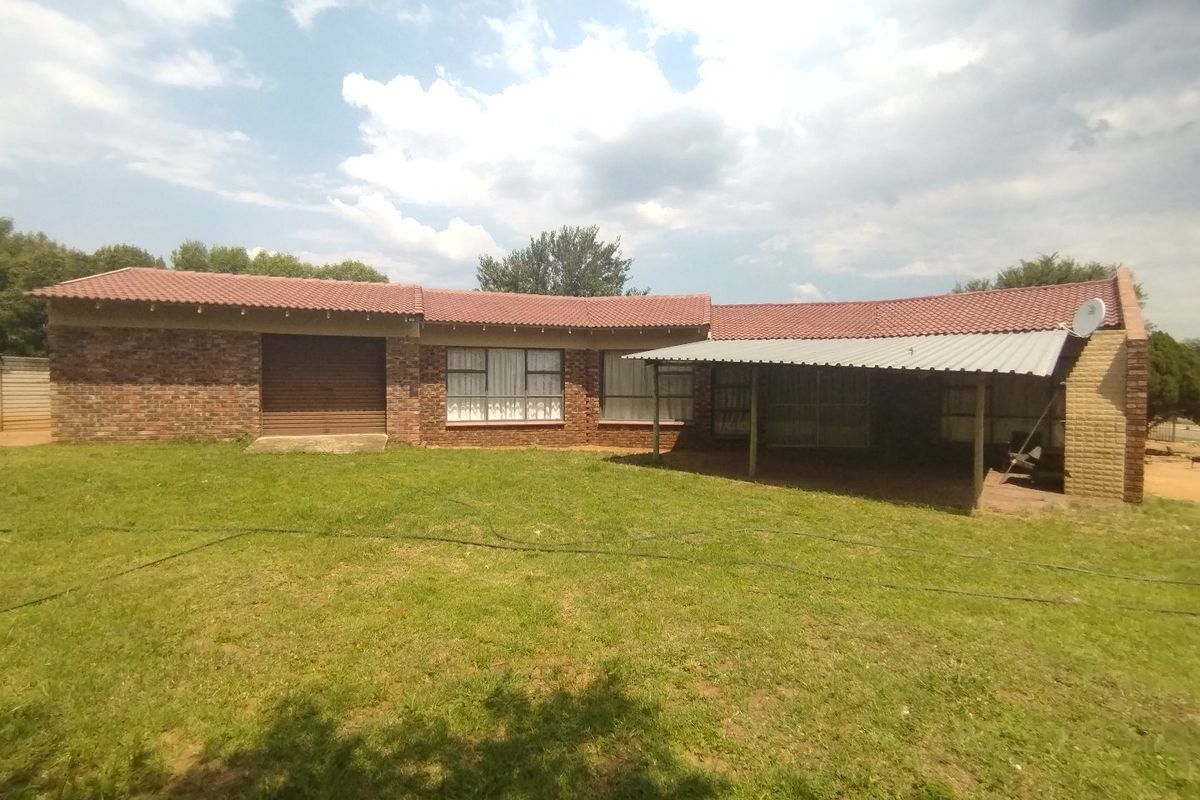 Rear view of a single-story brick house featuring a tiled roof, an attached garage, and a covered patio area overlooking the garden.