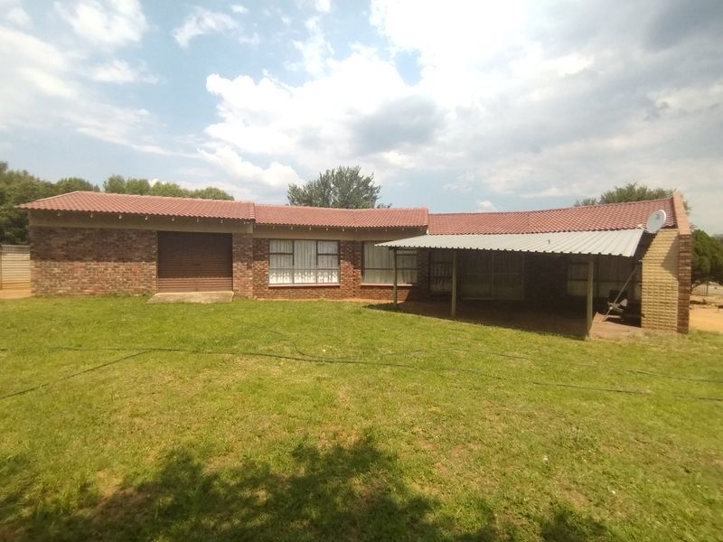 Rear view of a single-story brick house featuring a tiled roof, an attached garage, and a covered patio area overlooking the garden.