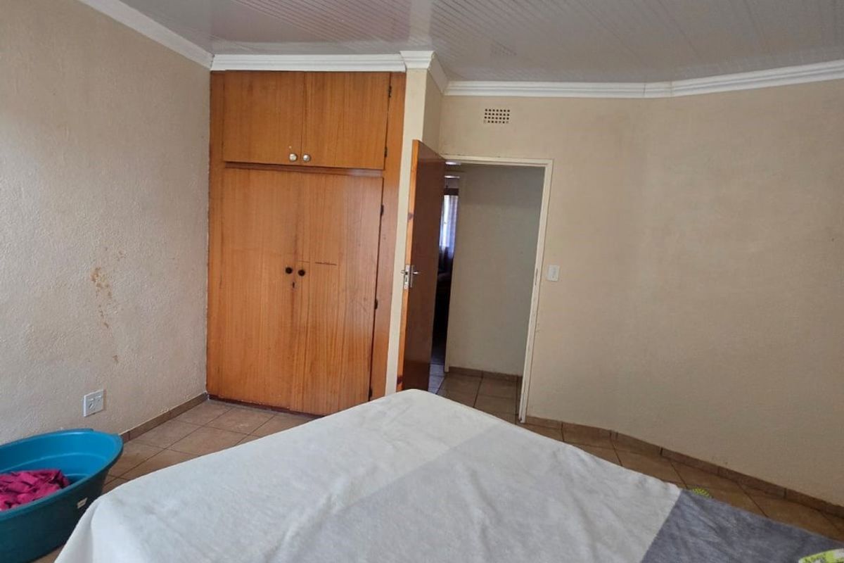 A bedroom featuring tiled flooring, a built-in wooden wardrobe, and a coved ceiling. The room requires cosmetic updates to the wall finishes.