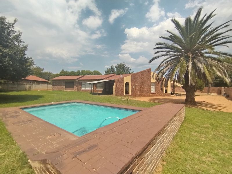 Rear view of the property featuring a swimming pool with brick coping, a spacious lawn, and a covered patio area.