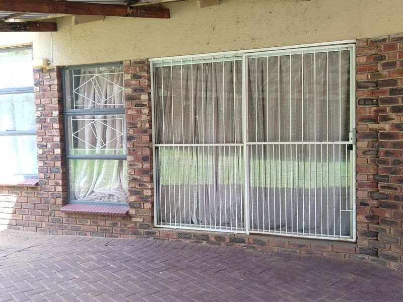 A covered patio area featuring face brick walls, paved flooring, and security gates over the windows and sliding doors.