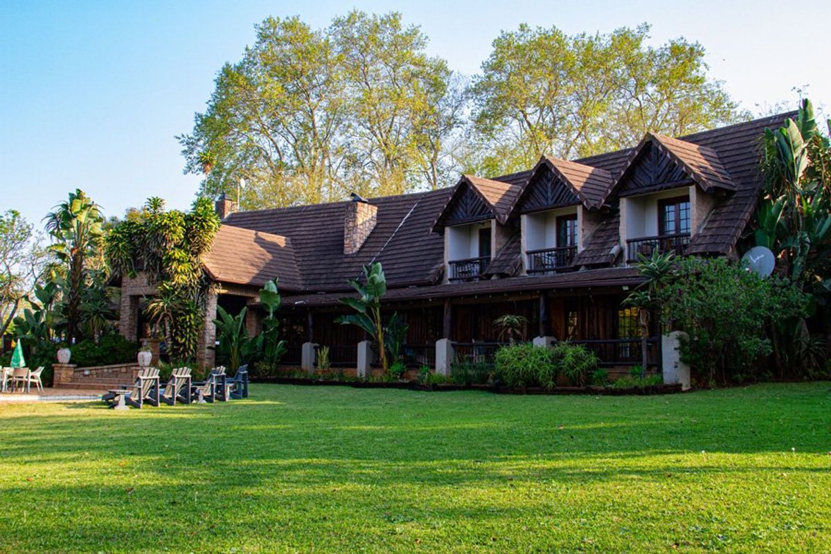 A spacious rear exterior view of a multi-story commercial property featuring a large lawn, covered patio, and timber balconies under a tiled roof.