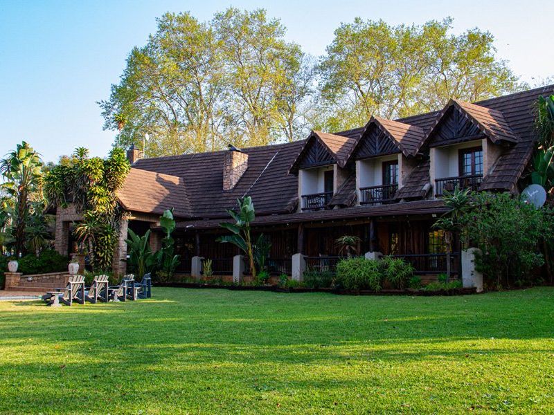 A spacious rear exterior view of a multi-story commercial property featuring a large lawn, covered patio, and timber balconies under a tiled roof.
