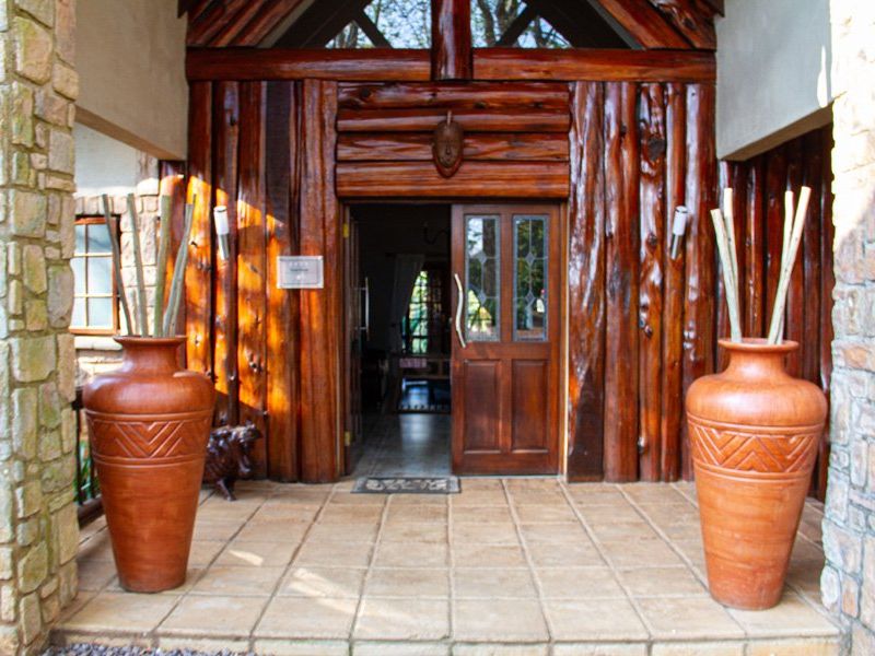 A rustic entrance featuring natural timber log cladding, stone masonry accents, and a tiled porch leading to a leaded glass front door.