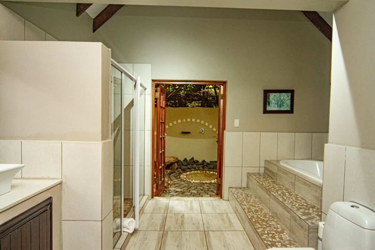 Spacious bathroom featuring a raised bathtub with pebble detailing, a glass-enclosed shower, and direct access to a private outdoor area.