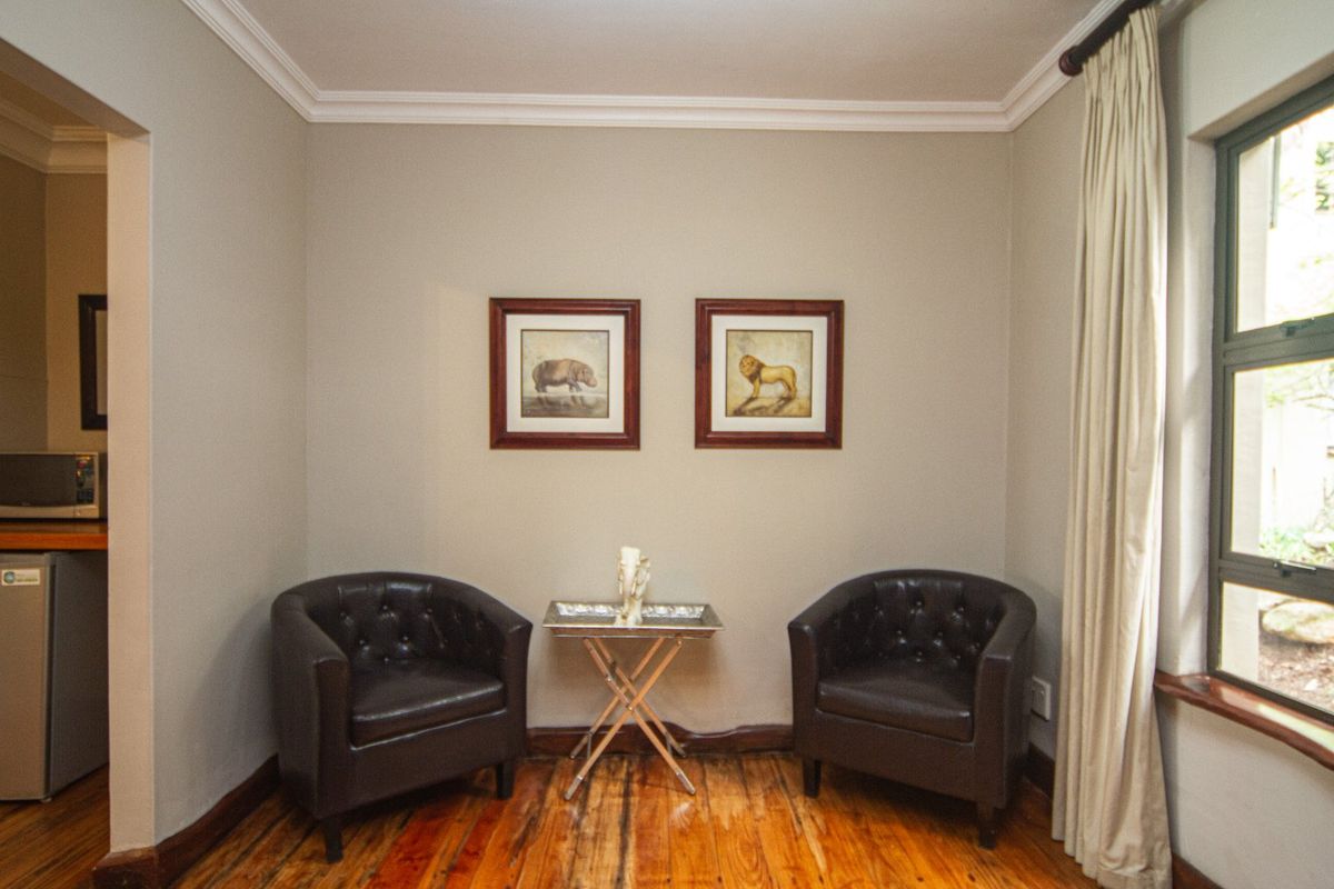 A cozy seating area featuring polished timber flooring, decorative cornice, and a large window with natural light.