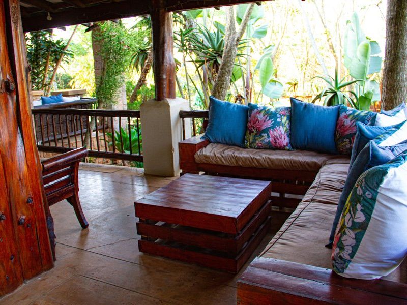 A covered outdoor patio area featuring rustic timber support columns, concrete flooring, and a wooden railing overlooking a lush garden setting.