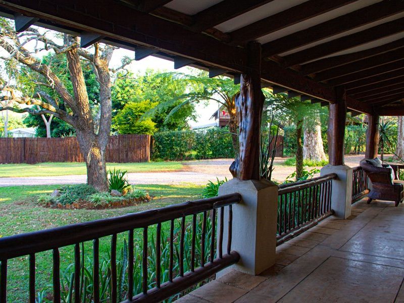 A covered outdoor patio featuring rustic timber support posts, exposed beam ceiling, and a timber railing overlooking a landscaped garden area.