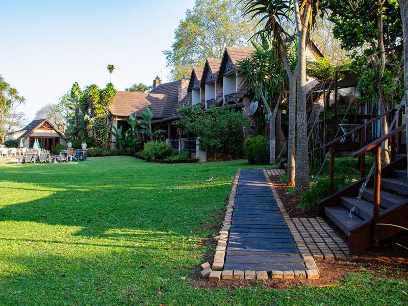 A spacious rear garden area featuring a timber walkway, landscaped greenery, and access to the main building structure with a tiled roof.
